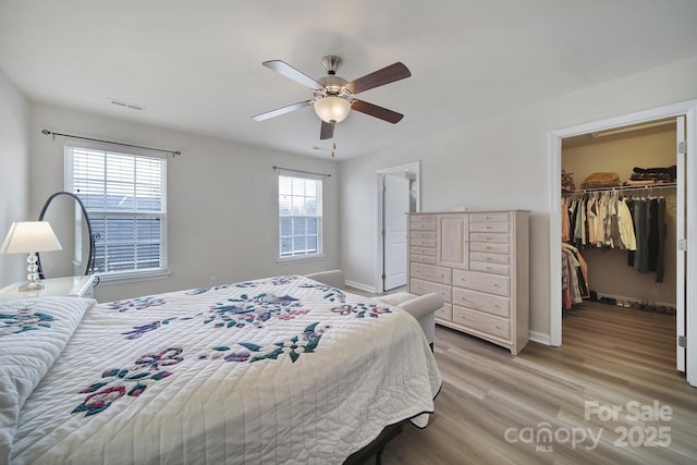 bedroom with a walk in closet, a closet, visible vents, light wood-style flooring, and baseboards