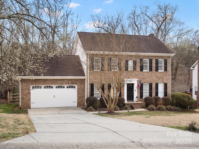 colonial home with a garage, brick siding, driveway, roof with shingles, and a chimney