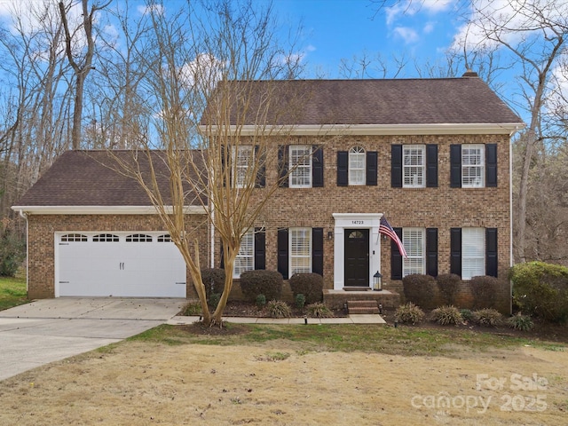 colonial house with a garage, brick siding, driveway, and a shingled roof