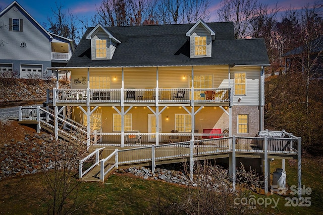 back of house at dusk featuring a balcony and roof with shingles