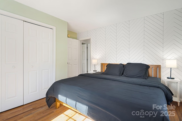 bedroom with wallpapered walls, wood finished floors, an accent wall, and a closet