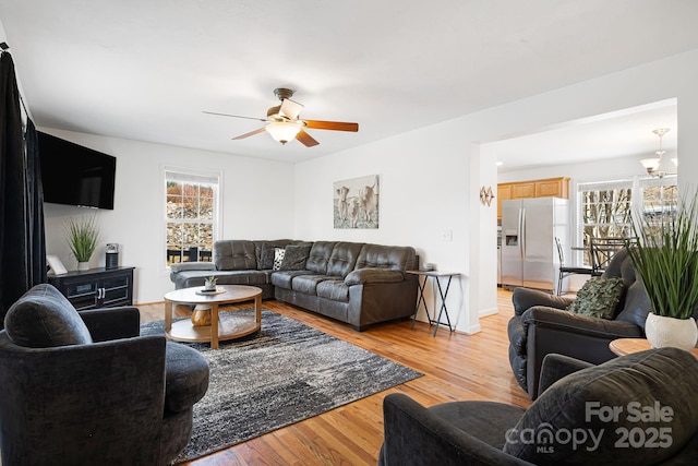 living area featuring ceiling fan, baseboards, and light wood-style flooring