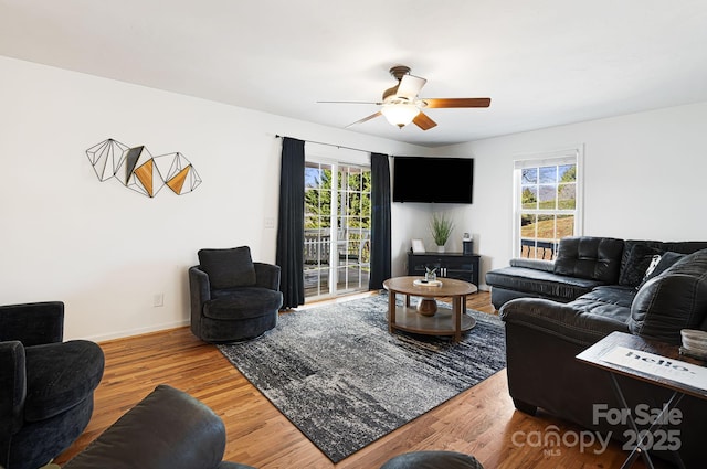 living room featuring baseboards, a ceiling fan, wood finished floors, and plenty of natural light