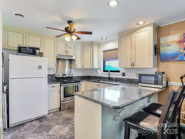 kitchen with appliances with stainless steel finishes, cream cabinetry, a sink, and under cabinet range hood