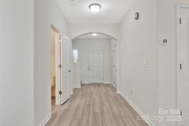 hall featuring light wood-type flooring, arched walkways, and baseboards