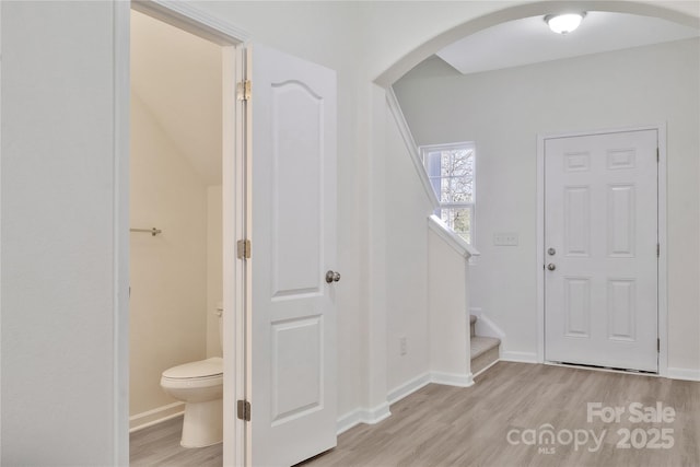 foyer with arched walkways, light wood finished floors, stairs, and baseboards