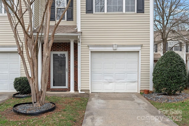 doorway to property featuring a garage, brick siding, and driveway