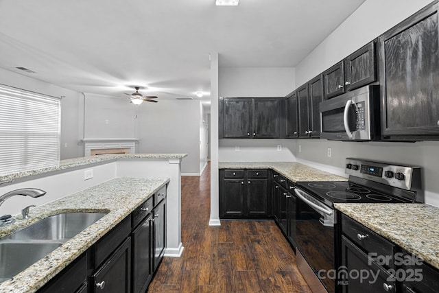 kitchen featuring a sink, dark cabinetry, dark wood finished floors, appliances with stainless steel finishes, and light stone countertops