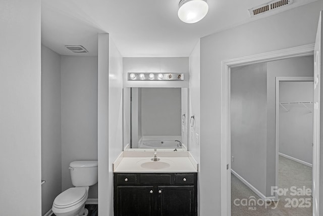 bathroom featuring visible vents, a walk in closet, baseboards, toilet, and vanity