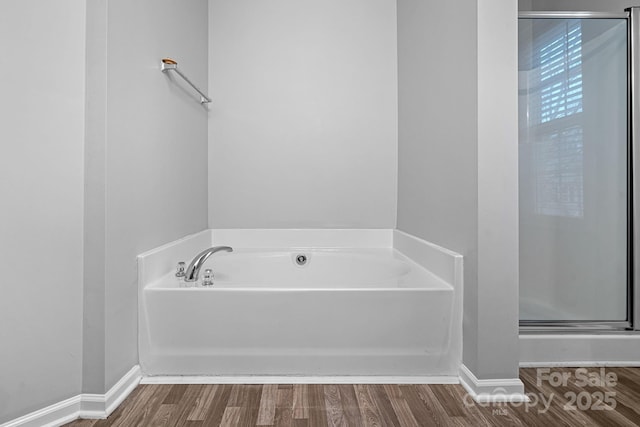 bathroom with baseboards, wood finished floors, a garden tub, and a stall shower