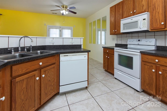 kitchen with light tile patterned floors, white appliances, a sink, backsplash, and brown cabinets