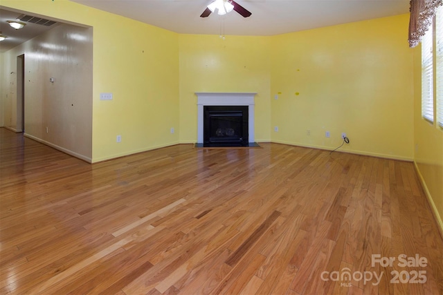 unfurnished living room featuring visible vents, light wood-style flooring, a fireplace with flush hearth, a ceiling fan, and baseboards