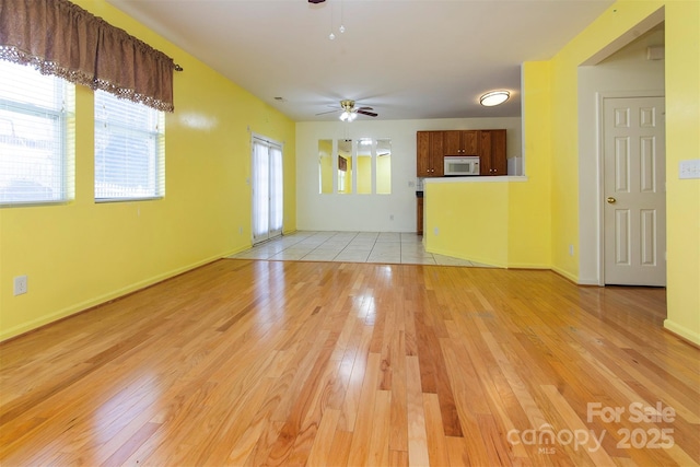 unfurnished living room with light wood finished floors, a ceiling fan, and baseboards