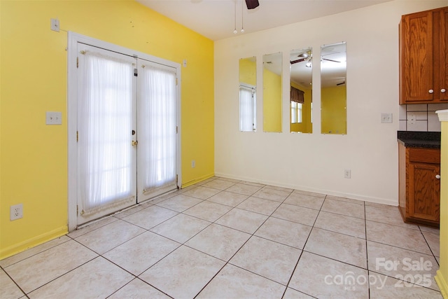 unfurnished dining area featuring light tile patterned floors, ceiling fan, baseboards, and french doors