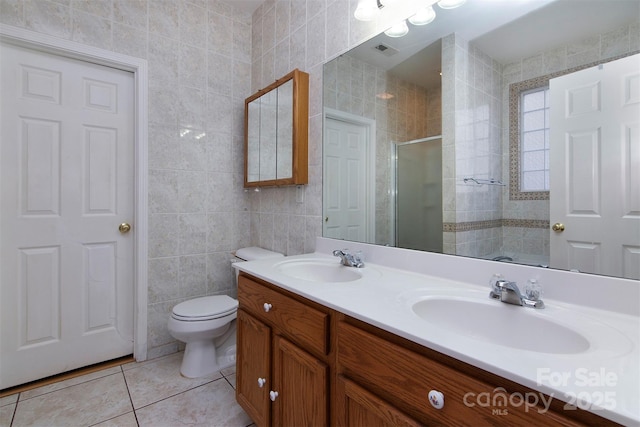 bathroom with a stall shower, tile patterned flooring, tile walls, and a sink