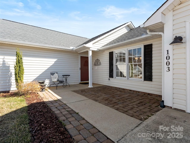 entrance to property with roof with shingles and a patio