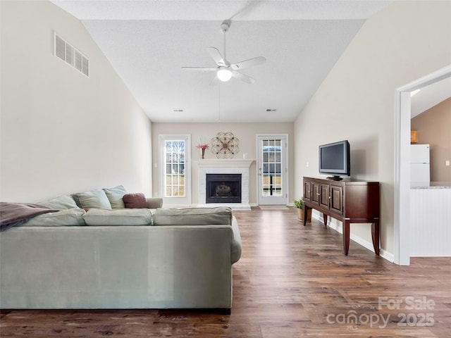 living room featuring visible vents, lofted ceiling, ceiling fan, dark wood-type flooring, and a fireplace