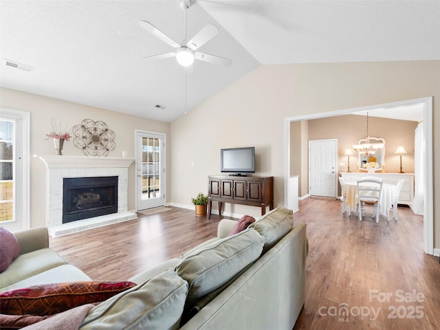 living room with visible vents, lofted ceiling, wood finished floors, a brick fireplace, and ceiling fan with notable chandelier