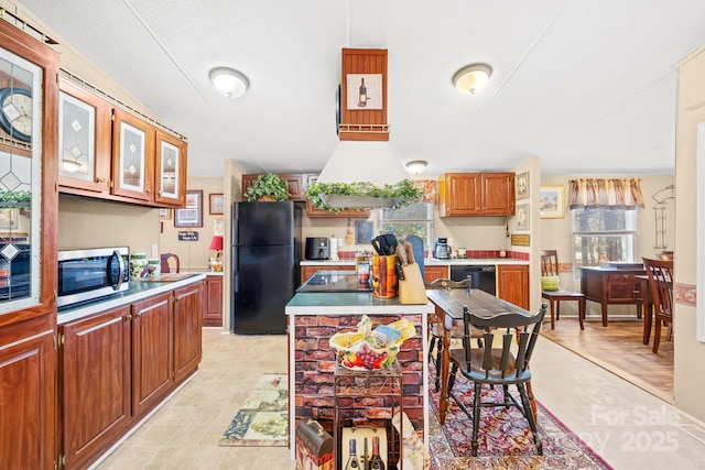 kitchen featuring black appliances, range hood, light countertops, and a sink