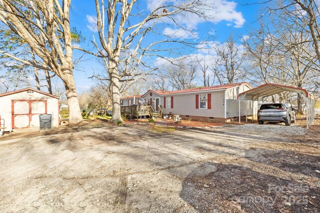 view of front facade with dirt driveway, crawl space, a storage unit, an outdoor structure, and a carport