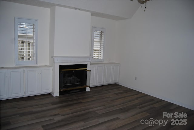 unfurnished living room featuring dark wood-style flooring, a glass covered fireplace, and baseboards