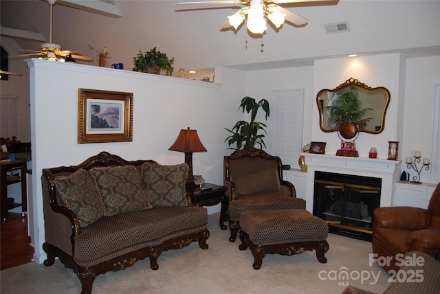 living area with a ceiling fan, a glass covered fireplace, visible vents, and carpet floors