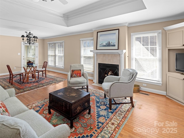 living area with visible vents, light wood-style floors, a tray ceiling, a tiled fireplace, and crown molding