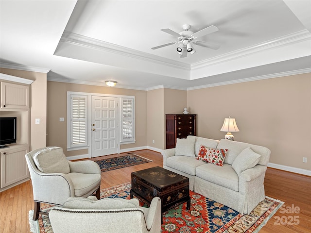 living room with a tray ceiling, baseboards, crown molding, and light wood finished floors