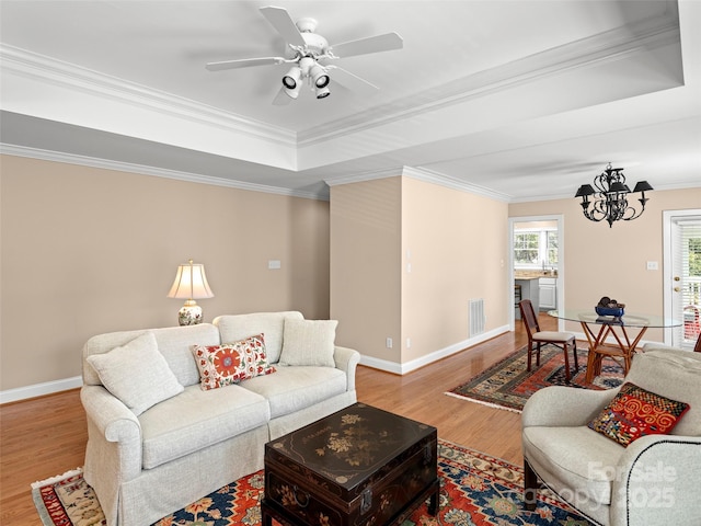 living area with crown molding, a raised ceiling, visible vents, wood finished floors, and baseboards