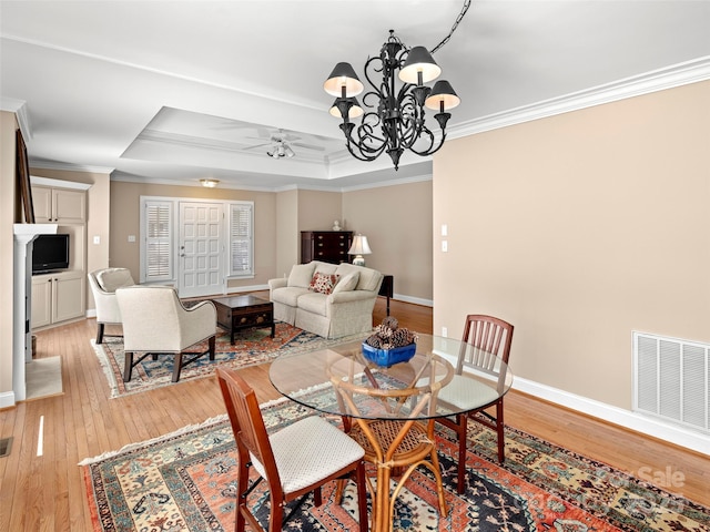 dining room featuring visible vents, baseboards, ornamental molding, a tray ceiling, and light wood finished floors