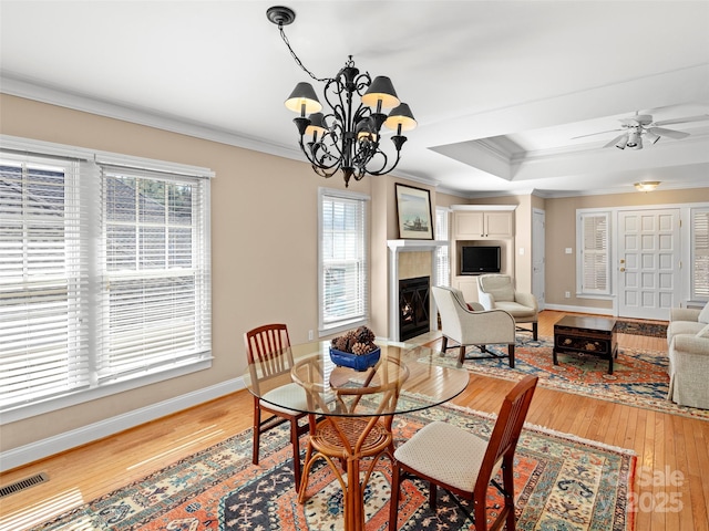 dining area with a warm lit fireplace, light wood-style flooring, visible vents, and crown molding