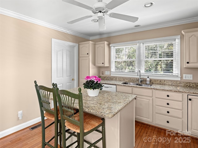 kitchen featuring white dishwasher, a breakfast bar, a sink, light wood finished floors, and crown molding