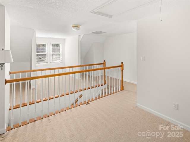 hall with baseboards, visible vents, vaulted ceiling, a textured ceiling, and carpet floors