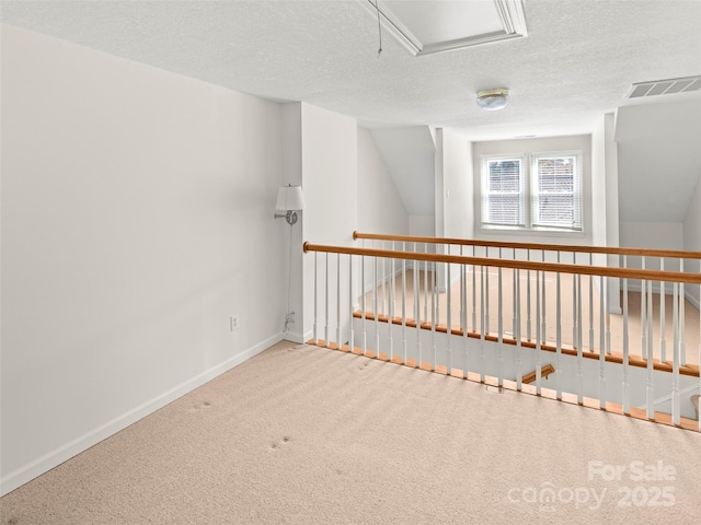 unfurnished room with a textured ceiling, lofted ceiling, visible vents, baseboards, and carpet