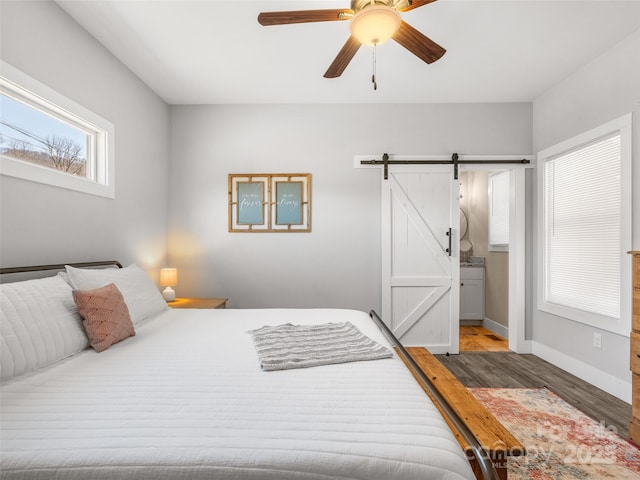 bedroom with a ceiling fan, a barn door, baseboards, and wood finished floors