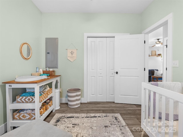 bedroom with a closet, electric panel, baseboards, and wood finished floors