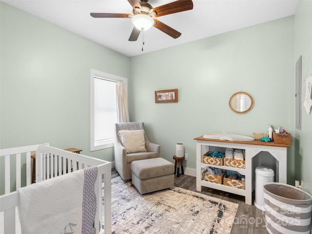 bedroom featuring a nursery area, wood finished floors, a ceiling fan, and baseboards