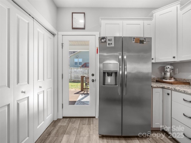 kitchen featuring light stone counters, light wood-type flooring, stainless steel fridge, and white cabinets