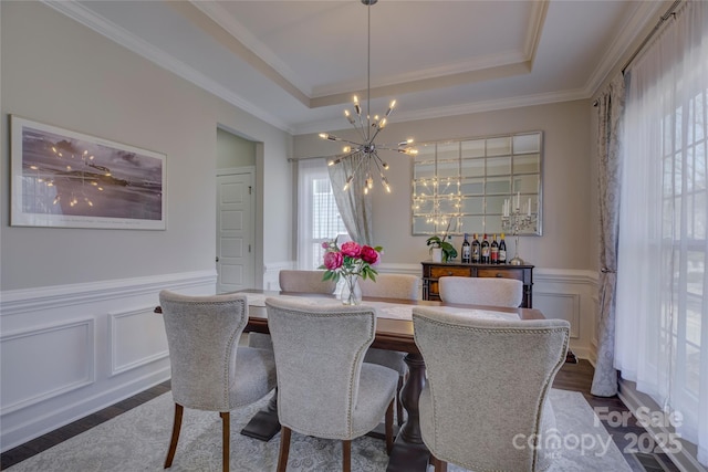 dining area with dark wood-type flooring, a tray ceiling, a chandelier, and a wainscoted wall