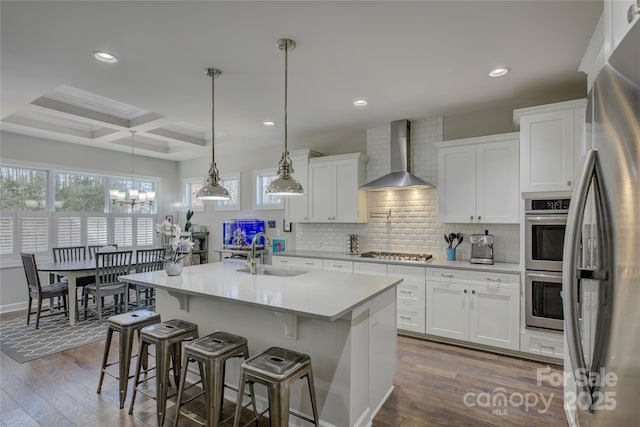 kitchen with tasteful backsplash, coffered ceiling, appliances with stainless steel finishes, wall chimney range hood, and a sink