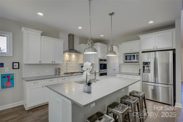 kitchen featuring dark wood finished floors, wall chimney exhaust hood, stainless steel appliances, white cabinetry, and a sink