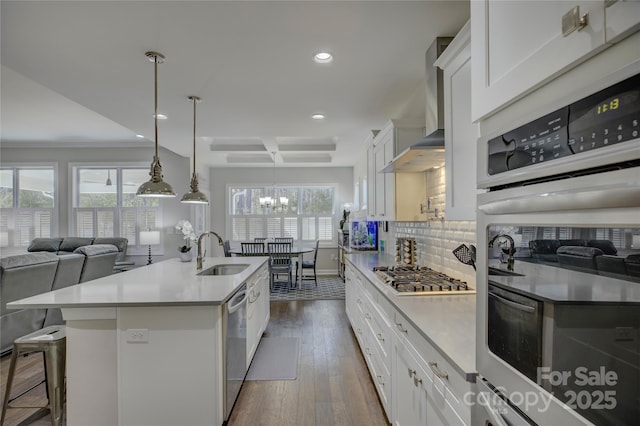 kitchen featuring tasteful backsplash, dark wood finished floors, wall chimney exhaust hood, stainless steel appliances, and a sink