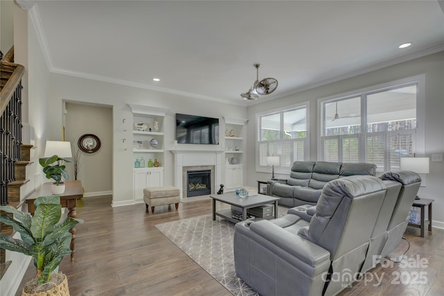 living area featuring built in features, crown molding, stairway, a glass covered fireplace, and wood finished floors