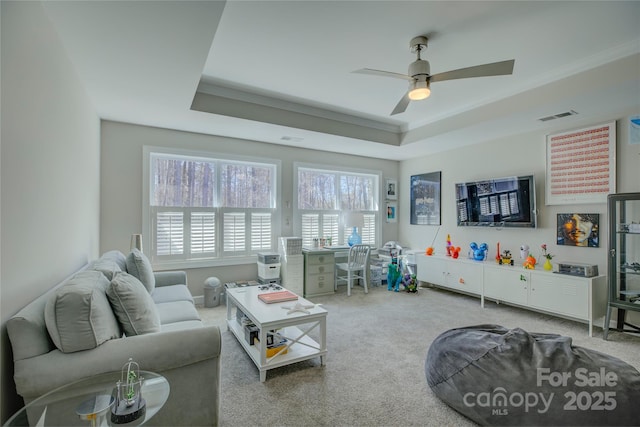 carpeted living area with crown molding, a raised ceiling, visible vents, and a ceiling fan