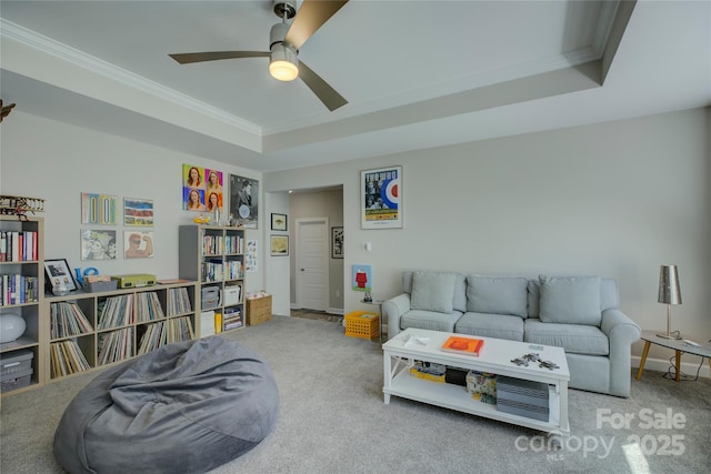 living area featuring a ceiling fan, carpet, a raised ceiling, and crown molding