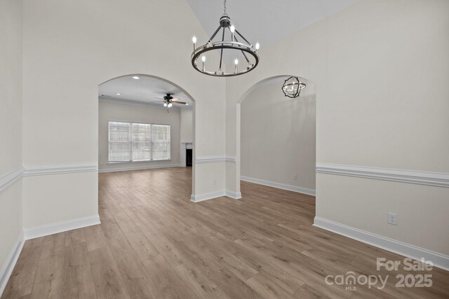 unfurnished dining area featuring arched walkways, ceiling fan with notable chandelier, wood finished floors, baseboards, and vaulted ceiling