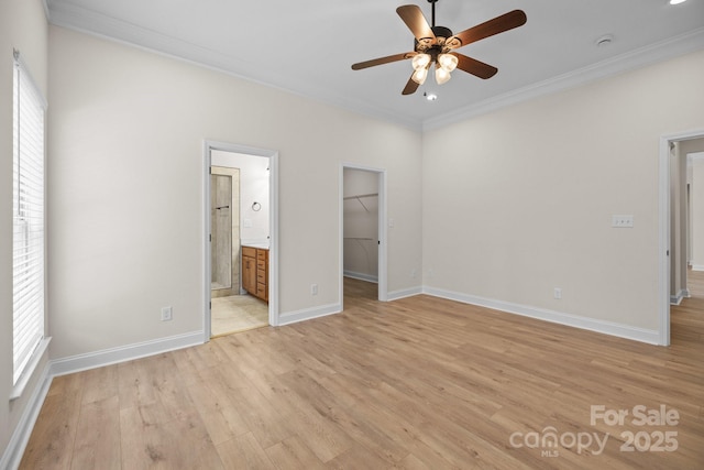 unfurnished bedroom featuring baseboards, a spacious closet, ornamental molding, a closet, and light wood-type flooring