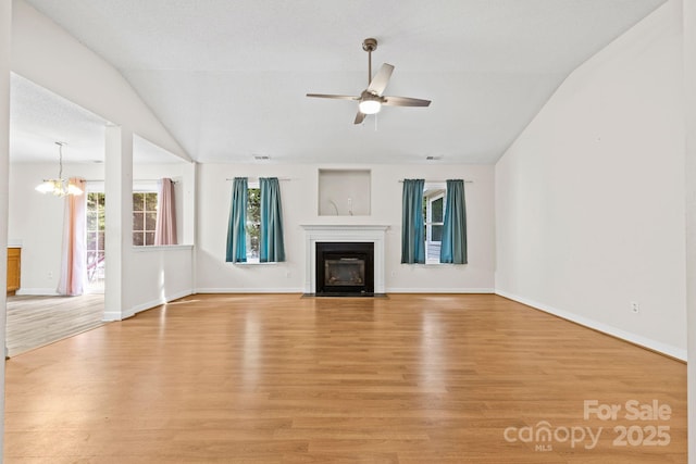 unfurnished living room featuring light wood-style flooring, a fireplace with flush hearth, vaulted ceiling, baseboards, and ceiling fan with notable chandelier