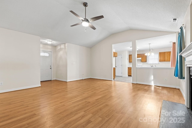 unfurnished living room featuring visible vents, a fireplace with flush hearth, light wood-style floors, vaulted ceiling, and ceiling fan with notable chandelier