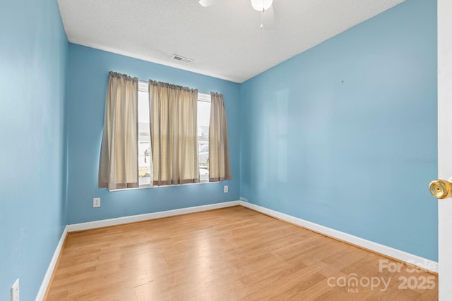 unfurnished room with a textured ceiling, wood finished floors, a ceiling fan, visible vents, and baseboards